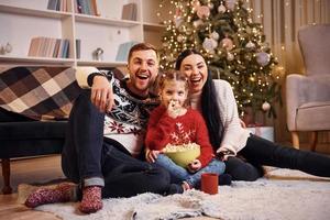 familia feliz adentro en una habitación decorada con navidad celebrando el año nuevo con palomitas de maíz foto