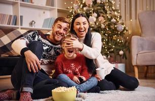 familia feliz adentro en una habitación decorada con navidad celebrando el año nuevo con palomitas de maíz foto