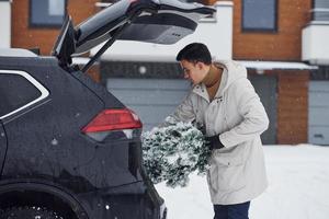 Man in white coat putting christmas fir tree inside his automobile photo