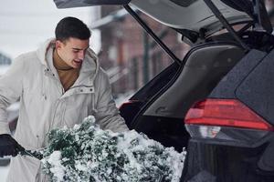 Man in white coat putting christmas fir tree inside his automobile photo