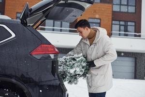 hombre en bata blanca poniendo abeto de navidad dentro de su automóvil foto