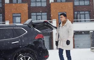 Young handsome man outdoors near his modern black car at winter time photo