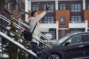 Man with christmas tree standing on the ladder of building near car photo