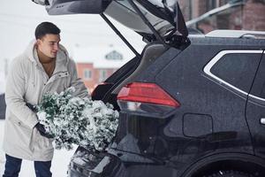 Man in white coat putting christmas fir tree inside his automobile photo