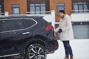 Young handsome man outdoors near his modern black car at winter time photo