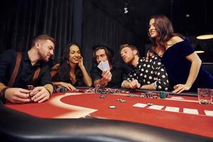 grupo de jóvenes elegantes que juegan al póquer en el casino juntos foto