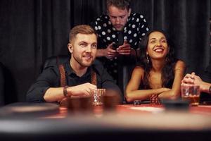 With glasses of drink. Group of elegant young people that playing poker in casino together photo