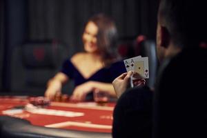 Elegant young people sits by table, playing poker in casino and checking their cards photo