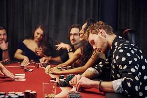 grupo de jóvenes elegantes que juegan al póquer en el casino juntos foto