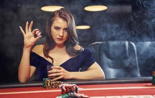 mujer con ropa elegante se sienta en cassino junto a la mesa y juega al póquer foto