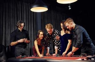People in elegant clothes standing and playing poker in casino together photo