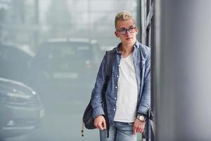 Young hipster guy in nice clothes stands indoors against grey background photo