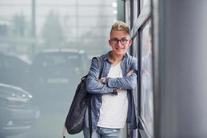 Young hipster guy in nice clothes stands indoors against grey background photo