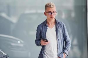 Young hipster guy in nice clothes stands indoors against grey background photo