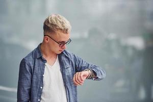 Young hipster guy in nice clothes stands indoors against grey background photo