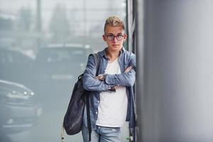 un joven hipster con ropa bonita se para en el interior contra un fondo gris foto