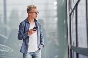 Young hipster guy in nice clothes stands indoors against grey background photo