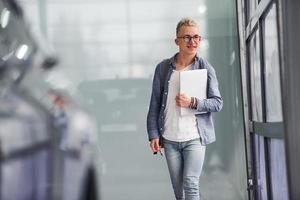 Young hipster guy in nice clothes stands indoors against grey background and near car photo