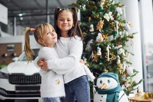 Two cute little girls standing near car and christmas tree at new year time photo