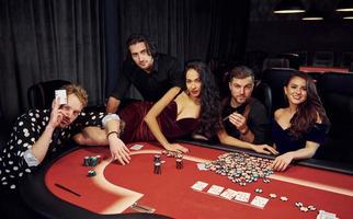 mujer acostada sobre la mesa. grupo de jóvenes elegantes que juegan al póquer en el casino juntos foto