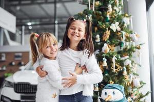 Two cute little girls standing near car and christmas tree at new year time photo