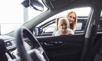 Mother and daughter looking inside modern new car in salon photo