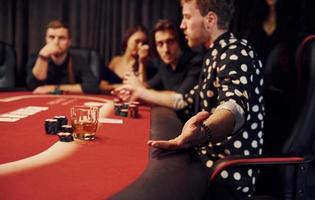 vista lateral del grupo de jóvenes elegantes que juegan al póquer en el casino juntos foto