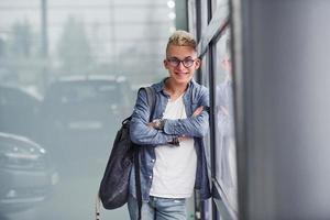 un joven hipster con ropa bonita se para en el interior contra un fondo gris foto