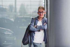 un joven hipster con ropa bonita se para en el interior contra un fondo gris foto