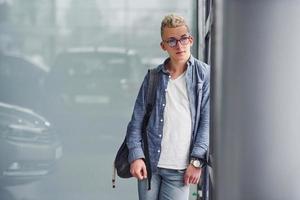 un joven hipster con ropa bonita se para en el interior contra un fondo gris foto