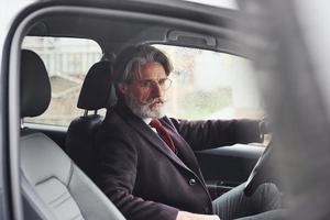 el hombre mayor de moda con ropa elegante está en el coche moderno foto