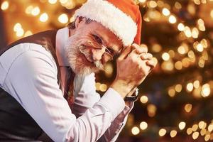 Portrait of stylish senior with grey hair and beard in jacket and white shirt is in decorated christmas room photo