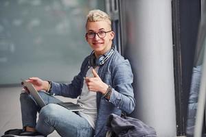 Young hipster guy in nice clothes sitting indoors near grey background photo