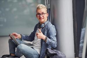 joven hipster con ropa bonita sentado en el interior cerca de un fondo gris foto