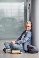 Young hipster guy sitting indoors near grey background with books photo