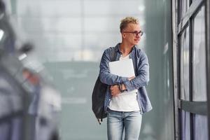 Young hipster guy in nice clothes stands indoors against grey background and near car photo