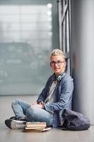 joven hipster sentado en el interior cerca de un fondo gris con libros foto