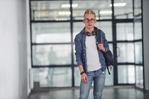 Young student in casual clothes walks indoors with backpack photo