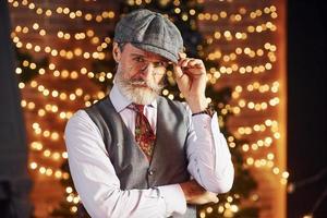 Portrait of stylish senior with grey hair and beard in jacket and white shirt is in decorated christmas room photo