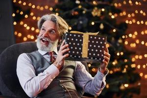 el retrato de un anciano elegante con cabello gris y barba está en una sala de navidad decorada con caja de regalo foto