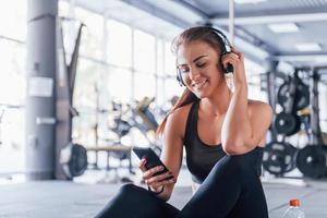 Young girl in sportive clothes and in headphones sitting in the gym at daytime photo