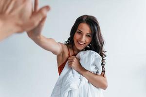 Positive beautiful young brunette in underwear in white room gives high five to the other person photo