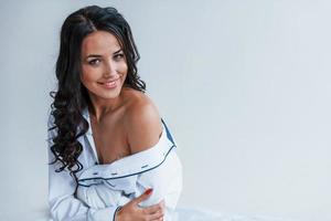 Beautiful young brunette in white coat stands in the studio photo