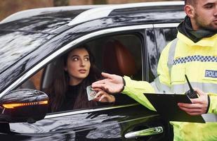 oficial de policía masculino con uniforme verde que acepta sobornos del conductor del vehículo en la carretera