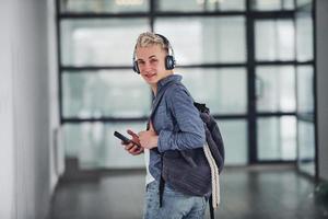 Young student in casual clothes walks indoors with backpack photo