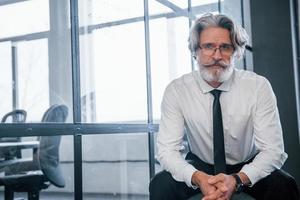 Portrait of mature businessman with grey hair and beard in formal clothes that sitting in the office photo