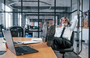 Senior businessman with grey hair and beard in formal clothes takes a break in the office photo