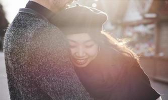 alegre pareja multirracial abrazándose al aire libre en la ciudad. chica asiática con su novio caucásico foto