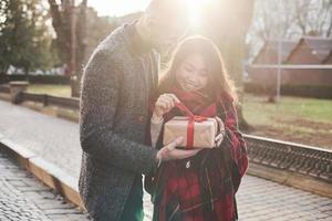 hermosa luz del sol. feliz pareja multirracial juntos al aire libre en la ciudad con caja de regalo en las manos foto