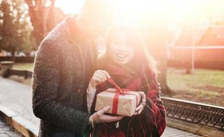 Beautiful sunlight. Happy multiracial couple together outdoors in the city with gift box in hands photo